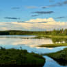 A lake is shown with trees in the background and the water is calm.