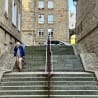 An older woman is using a cell phone while walking down a set of stairs.