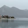 A boat is on the water in front of a small town with mountains in the background.