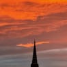 A tall tower with a pointy top and a dark silhouette against a pinkish sky.
