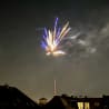 A firework explode in the sky above a building with a window.