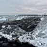 A beach scene with clear ice and rocks, and a person in the distance.