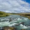 A picture of a river with a waterfall shown with clouds in the background.
