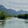 A river flows through a lush green forest, with mountains in the background.