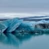 A large block of ice breaks off from a body of water and floats on top.
