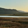 A beautiful view of a lake and mountains with a small cabin in the middle of the wilderness.