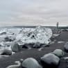 A person walking on a beach with large chunks of ice scattered around them.