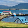 A blue house sits in a grassy field next to a body of water.