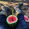 A person is sitting down and eating a watermelon slice that is in the shape of a spoon.