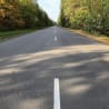 An empty road with white stripes in it that goes on for miles and has trees in the background.