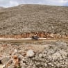 A person on a motorcycle is riding down a dirt road next to a large pile of rocks.