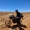 A man is standing next to his motorcycle in the middle of the desert.