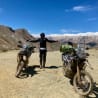 A man standing between two motorcycles in the dirt with his arms up.