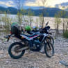 a motorcycle with a green bag on it next to a body of water.