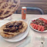 A plate of salad and a plate of meat are on a table with a can of soda between them.
