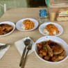A table with four bowls of food and silverware on it.