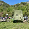 A green tent is set up next to a motorcycle on a grassy field.
