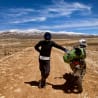 A man stands next to his motorcycle on a dirt road.