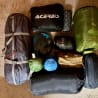 Several pieces of camping gear are spread out on a carpeted floor, including an Acecobis bag.