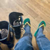 Two people with flip flops and boots sitting on a floor.
