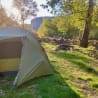 A tent is pitched in a grassy area with trees in the background.