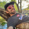 A man in a black shirt is lying in a hammock and taking a selfie.