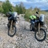 Two motorcycles are parked on a rocky path with their riders.