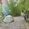 A tent is set up in a wooded area with a motorcycle parked nearby.