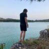 A man standing on rocks next to a body of water with a fish on a hook in his hand.