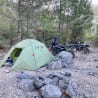 Two motorcycles are parked next to a tent on a rocky campsite.