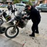 A man works on a motorcycle in a parking lot, with other vehicles around him.