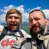 Two men wearing backpacks taking a picture together under a blue sky.