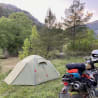 A motorcycle is parked next to a tent on a grassy area by a river.