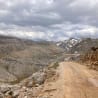 A dirt road winds through a mountain valley with clouds overhead.