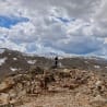 A man stands on a rocky mountain top under a cloudy sky.