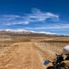 A motorcycle is parked on a dirt road with a mountain in the background.