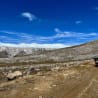 A dirt road winds through a rocky, mountainous pass with a green truck in the foreground.