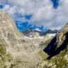 An alpine landscape with a mountain range and a valley between them, with snow on the mountainside.