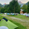 Several tents are pitched on a grassy area with mountains in the background.
