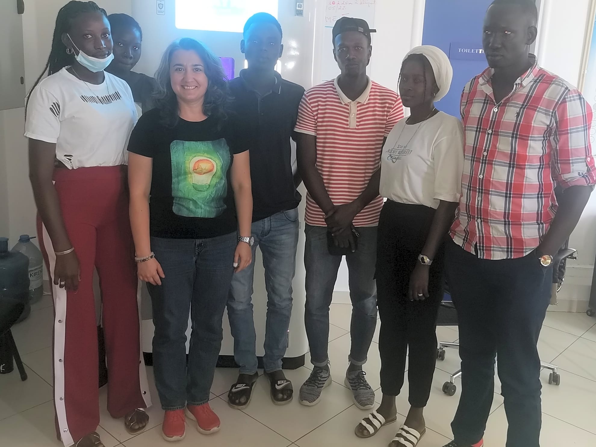 Директор по маркетингу и группа молодых сотрудников позирует на фоне автомата для воды в офисе в Сенегале