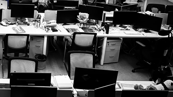 Черно-белое фото пустого офиса с рядами столов и мониторов, символизирующее безличную корпоративную среду, в которой рождаются шаблонные подарки.