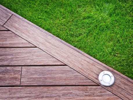 Der Rand einer Holzterrasse mit eingebautem Licht und einem Rasen daneben