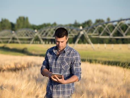 Landwirt mit Tablet vor Feld und Center Pivot Anlage