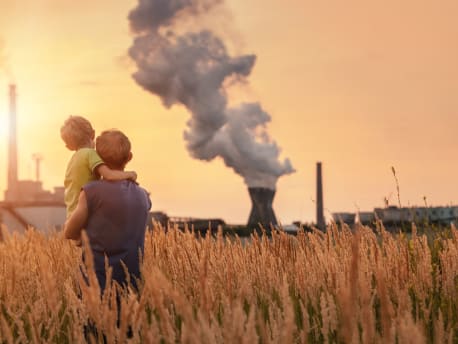 Mann mit Kind blickt auf ein Atomkraftwerk in der Ferne.