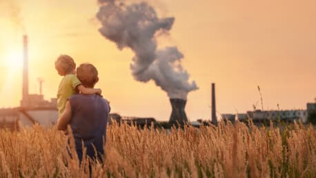 Vater mit Kind auf dem Arm blickt auf ein aktives Atomkraftwerk in der Ferne.