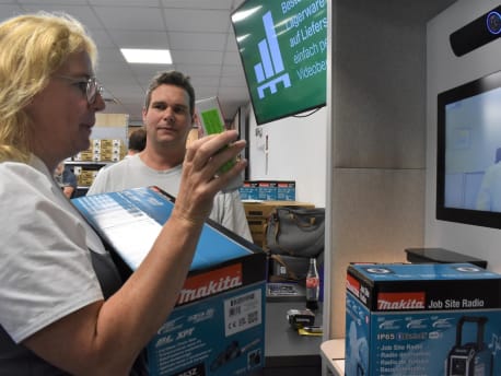 Frau und Mann stehen mit BayWa-Produkten vor einem Bildschirm und unterhalten sich