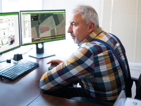 Elderly man sitting in front of two computer screens and using NEXT Farming software