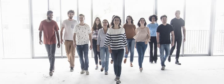 The picture shows a group of people happily walking towards the photographer in a large hall.