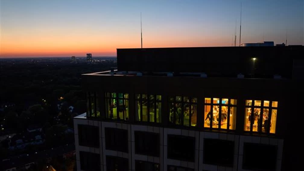 The picture shows the BayWa headquarters at dusk. Through a brightly lit window, the evening celebration of Charging Night can be seen from a distance.