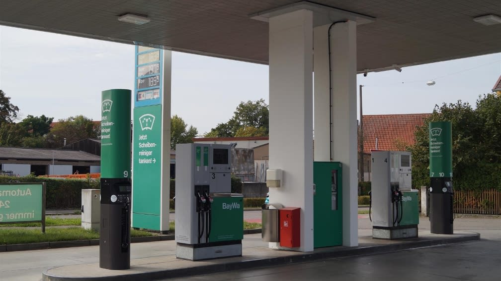 Ansicht einer Tankstelle mit Zapfsäulen und einer schlanken grünen EcoTank-Säule mit schwarzem Sockel.